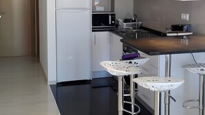 Eine moderne Küche mit weißen Schränken, einer schwarzen Arbeitsplatte, einer Mikrowelle, einem Spülbecken und drei weißen Barhocker.