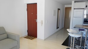 Ein modernes Wohnzimmer mit einer Couch, einer Holztür, einem Flur, der in eine Küche führt, und einem Essbereich mit Tisch und Stühlen.