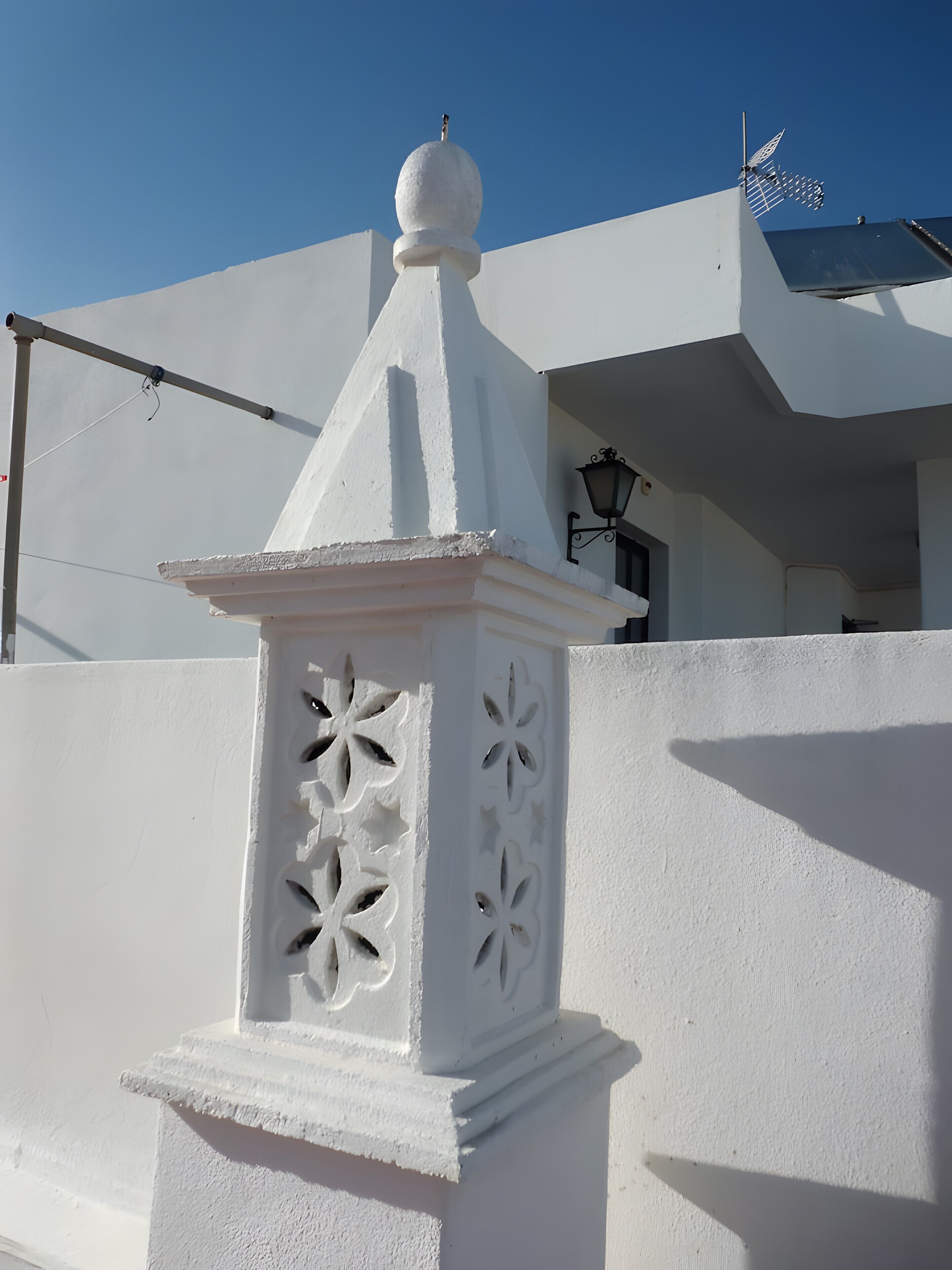 A white building with a decorative white fence, a pointed roof, and a clear blue sky.