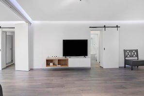 Ein modernes Wohnzimmer mit Flachbildfernseher, einer Holz-Unterhaltungsecke und einer Schiebetür zu einem weiteren Raum.