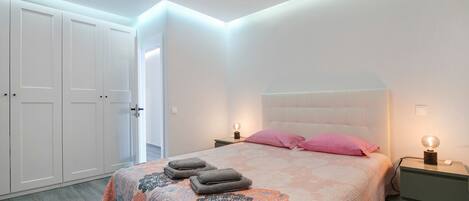 Un dormitorio con cama, dos mesitas de noche, un armario y una puerta.