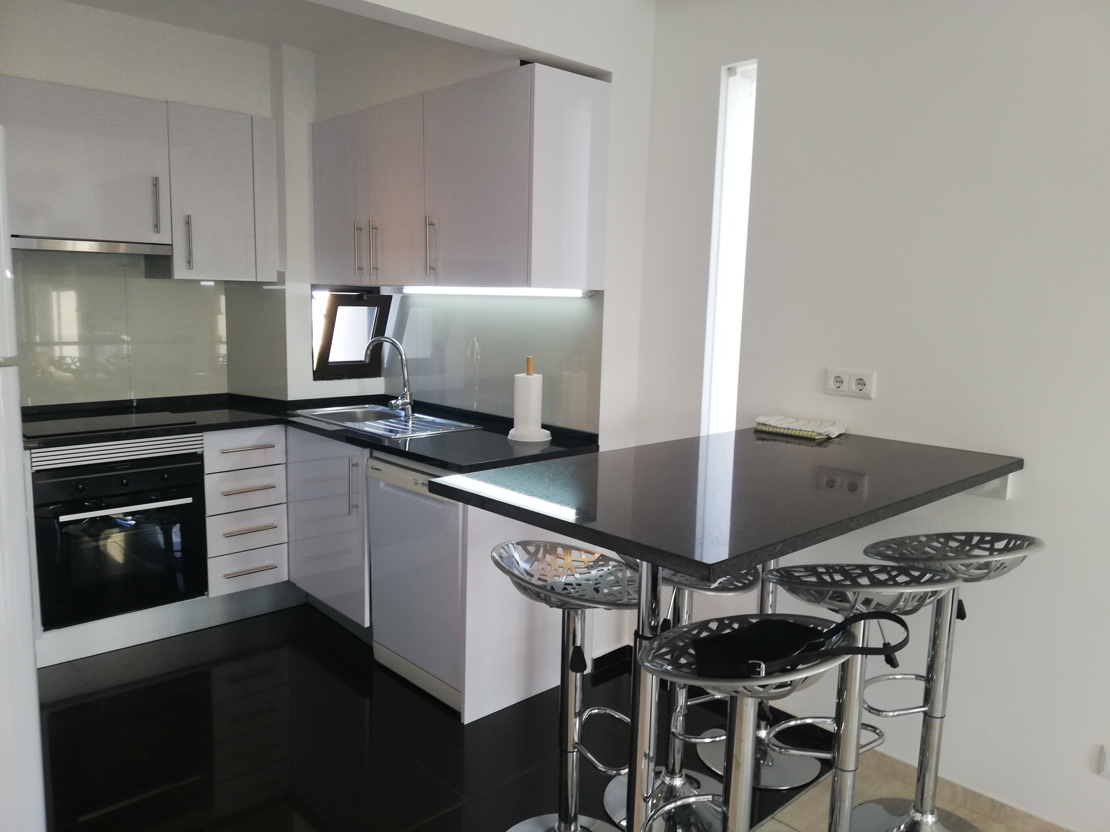 A modern kitchen with white cabinets, a black countertop, stainless steel appliances, and a bar stool area.