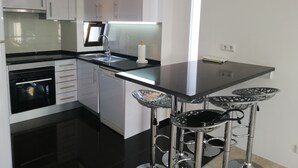 Une cuisine moderne avec des meubles blancs, un plan de travail noir, des appareils en acier inoxydable et un coin bar avec des tabourets.