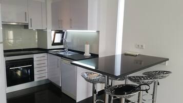 A modern kitchen with white cabinets, a black countertop, stainless steel appliances, and a bar stool area.