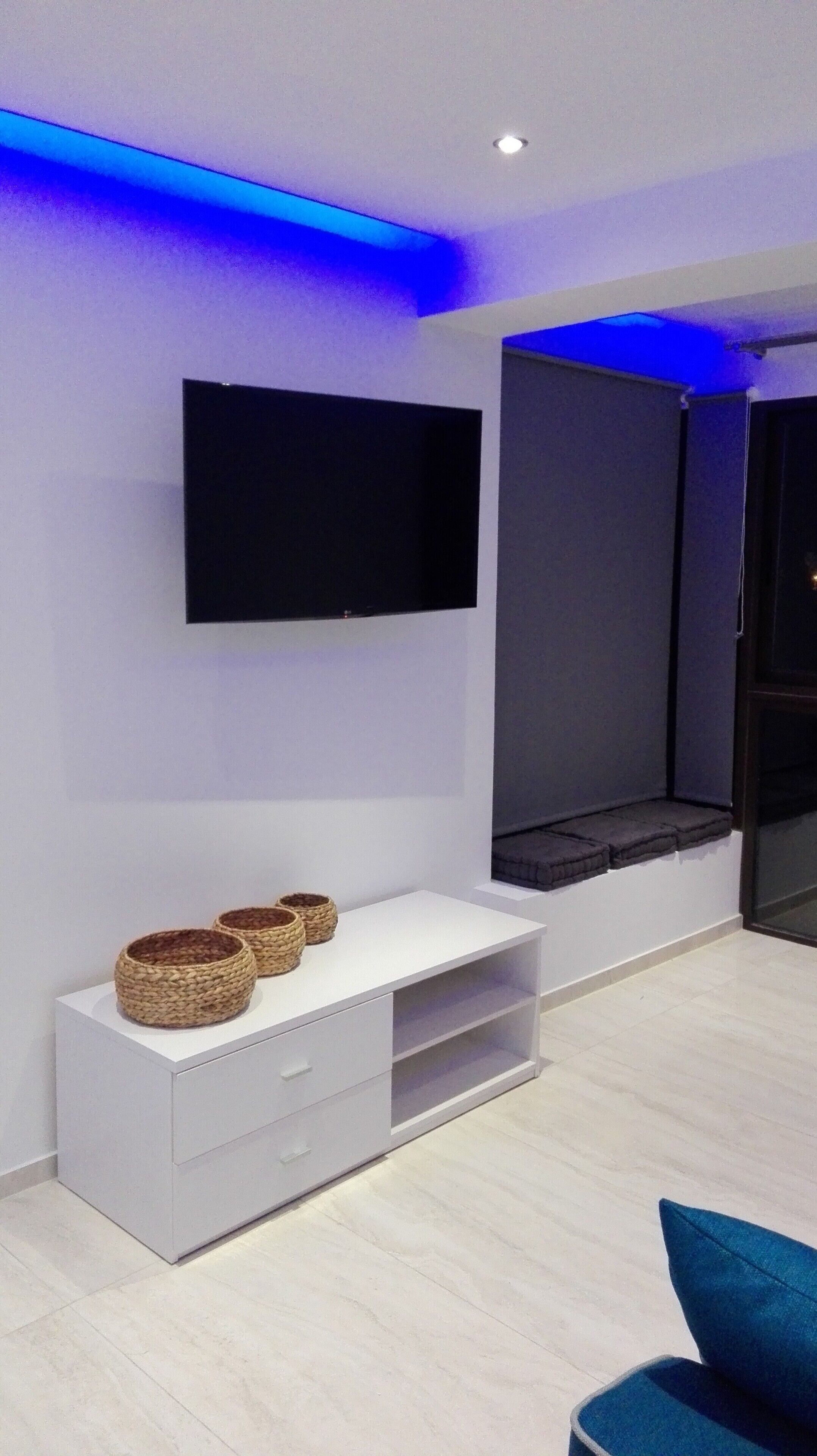 A modern living room with a flat-screen TV mounted on the wall, a white entertainment unit with baskets, and a blue accent wall.