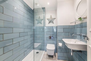 A bathroom with blue tiles, a glass shower enclosure, a white toilet, and a white sink. - The Bickley Mill Inn (Newton Abbot)