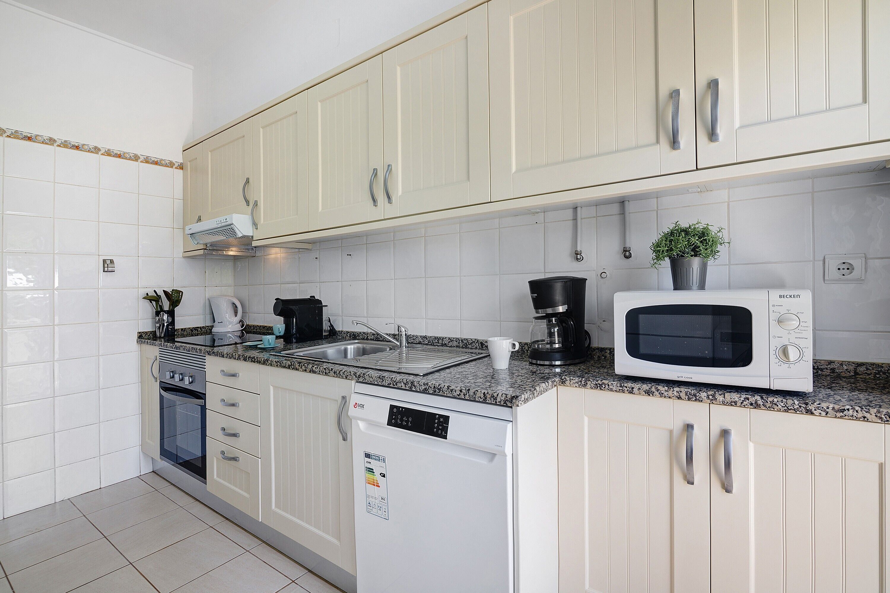 A kitchen with white cabinets, a dishwasher, a microwave, and a coffee maker.