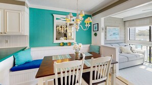 A dining area with a wooden table, white chairs, a teal accent wall, and a chandelier. - Our Place At The Beach 206G (Ocean City)