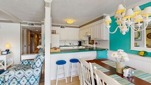 A kitchen with white cabinets, a dining area with a striped tablecloth, and a blue sofa. - Our Place At The Beach 206G (Ocean City)