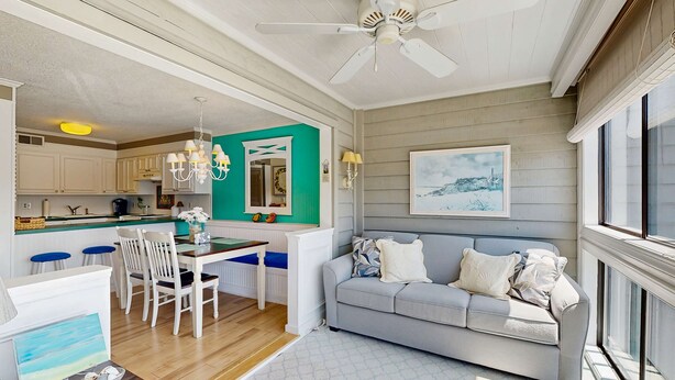 A modern kitchen with white cabinets, a dining area with a white table and chairs, a grey sofa, and a ceiling fan. - Our Place At The Beach 206G (Ocean City)