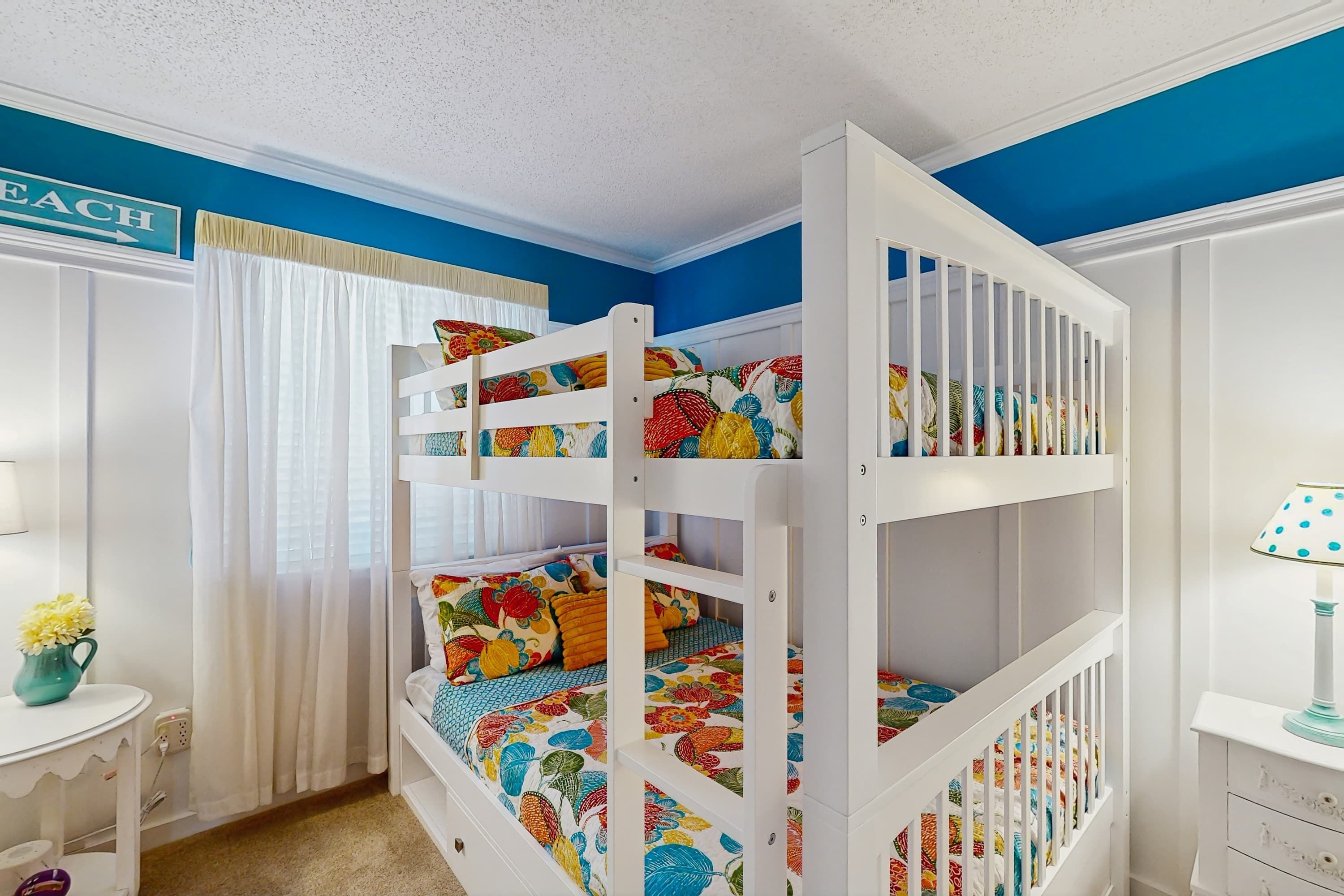 A bunk bed room with a blue wall, white ceiling, and a small desk with a lamp.