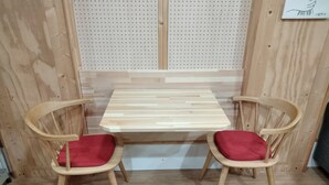 Um quarto com duas cadeiras de madeira com almofadas vermelhas, uma mesa de madeira e um painel de cortiça.