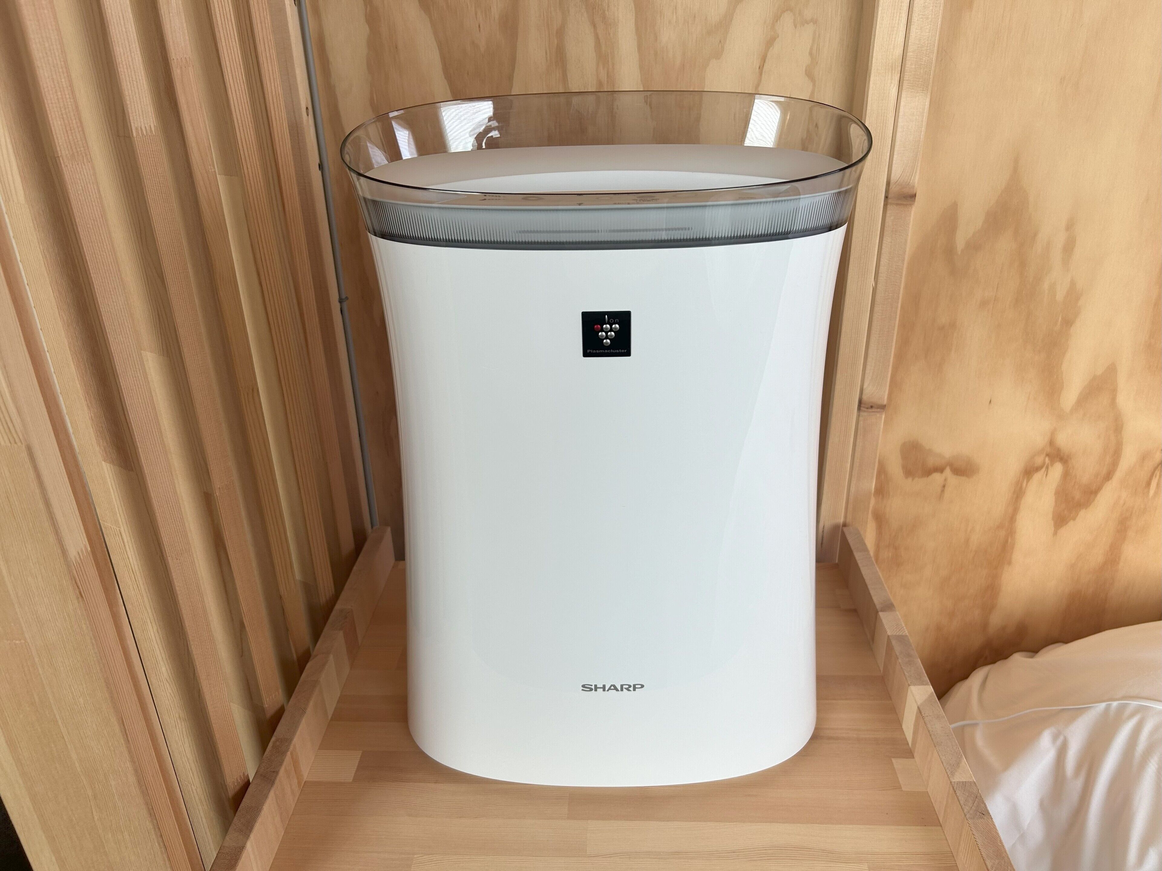 A white, cylindrical, glass-enclosed appliance with a control panel and the word 'SHARP' on it, placed on a wooden floor.