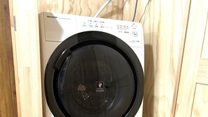 Máquina de lavar compacta, branca, em armário de madeira, com painel de controle e cabo de alimentação.