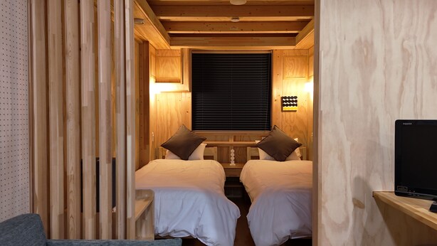Quarto de cabana de madeira com duas camas, uma janela com persianas e uma televisão sobre um suporte de madeira.