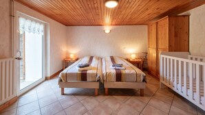 A room with two beds, a crib, wooden ceiling, and a window with curtains.