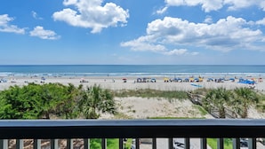 Blick auf einen Strand mit Palmen, einer Holzpromenade und Strandsonnenschirmen.