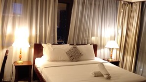 A hotel room with a large bed, two bedside lamps, and a view of the city at night through sheer curtains. - Berjaya Times Square Apartment (Kuala Lumpur)