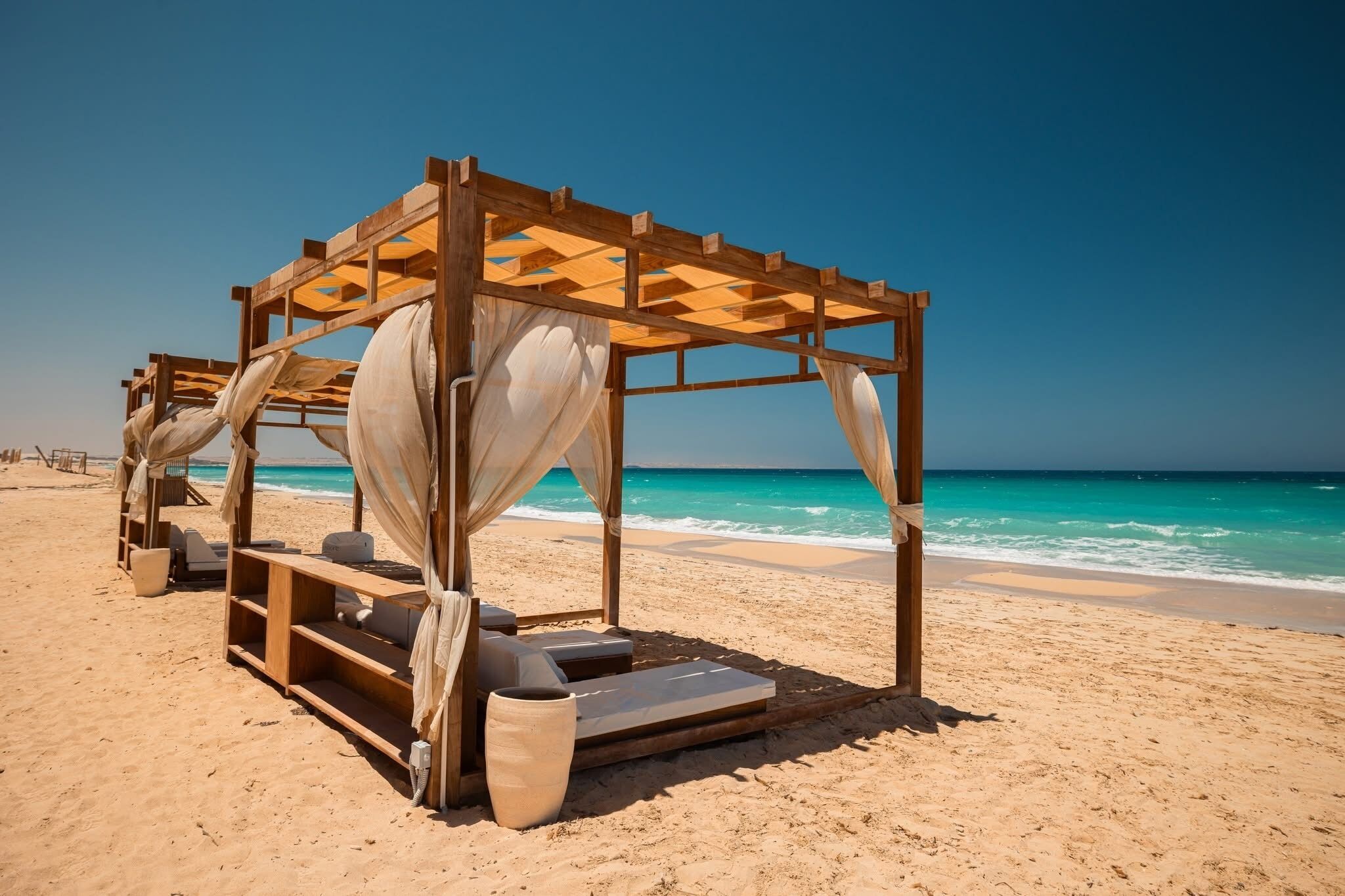A wooden beach cabana with a bench and a potted plant.