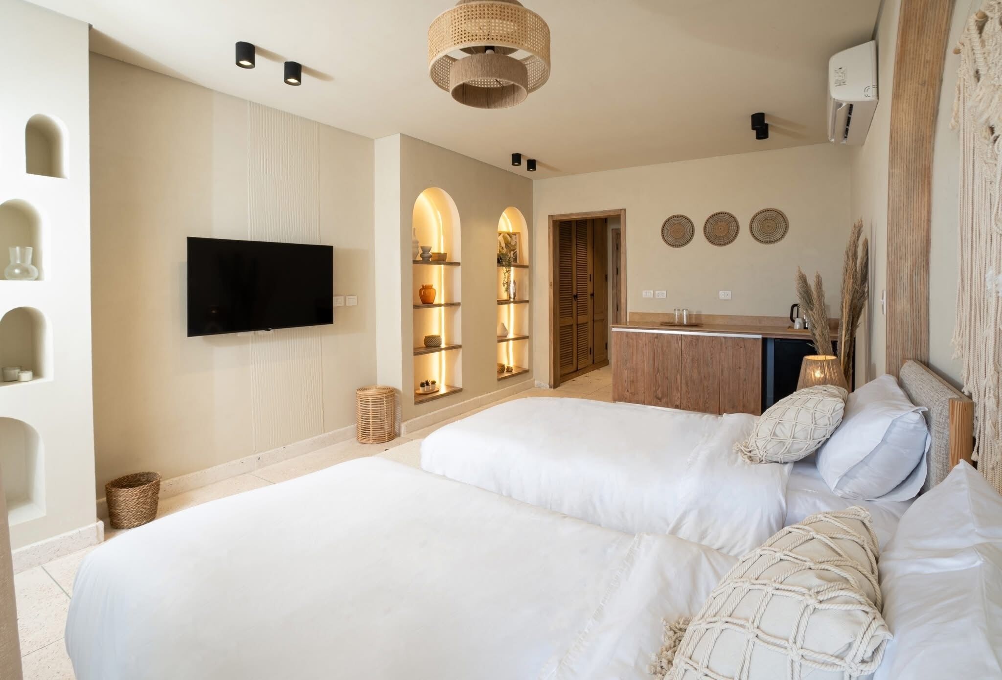 Une chambre moderne équipée d’une télévision, de deux lits, d’une commode en bois et d’une salle de bain avec un lavabo et un miroir.