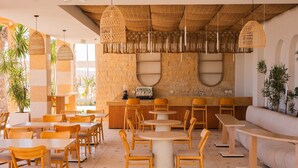 A restaurant with round tables and chairs, a bar area, and a seating area with a sofa. - Makai Hotel North Coast By Brassbell (El Dabaa)