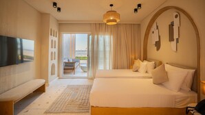 A hotel room with a large bed, a bench, a TV, and a view of the outdoors. - Makai Hotel North Coast By Brassbell (El Dabaa)