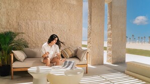 A room with a beige sofa, a round white table, and a view of the beach. - Makai Hotel North Coast By Brassbell (El Dabaa)