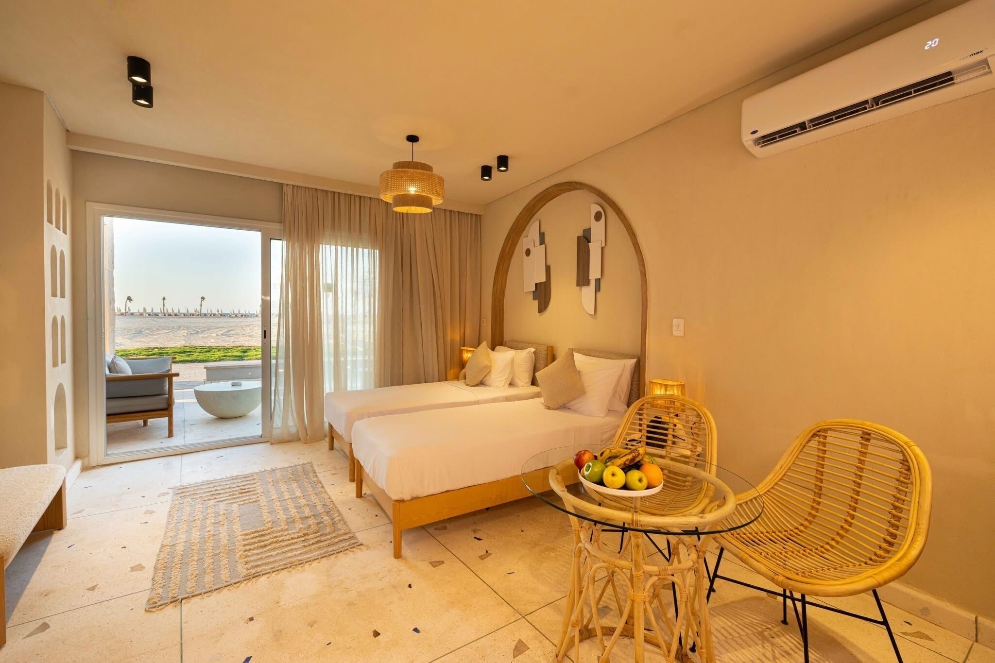 A hotel room with a bed, a dining table with chairs, a view through the window, and an air conditioning unit.