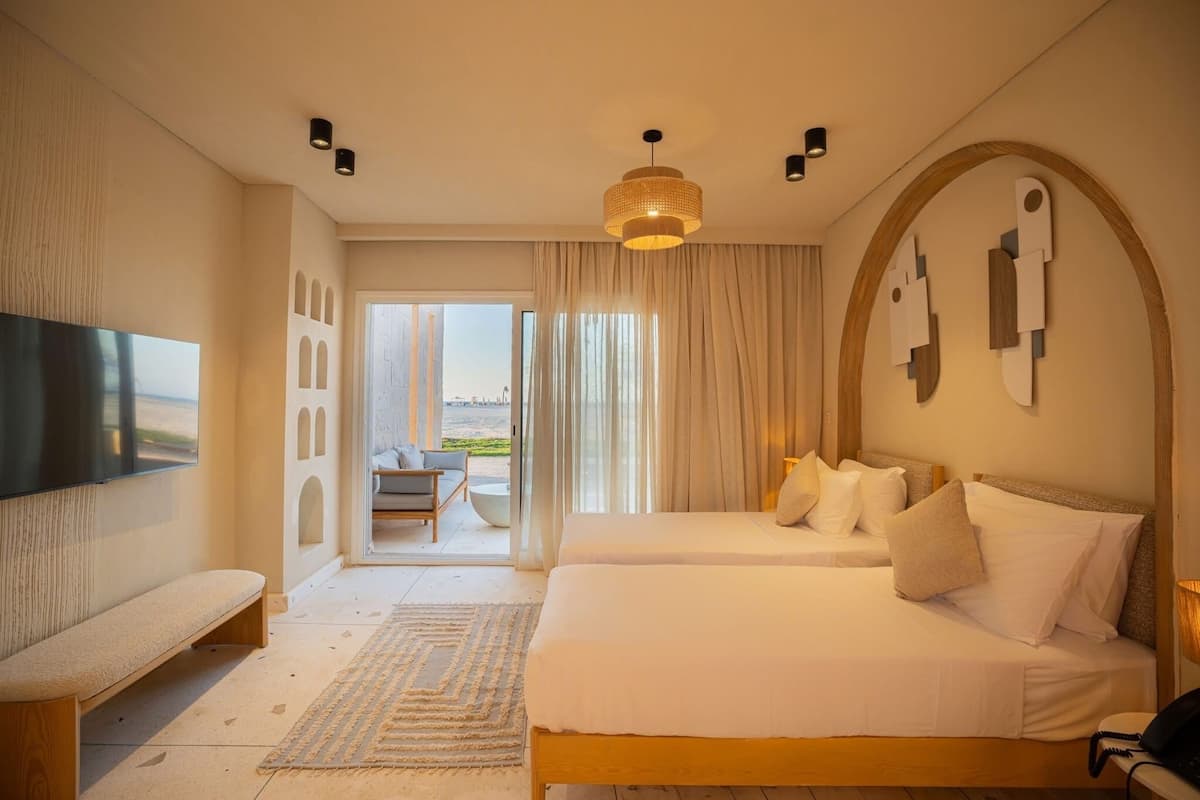 A hotel room with a bed, a bench, a TV, and a view of the outdoors.