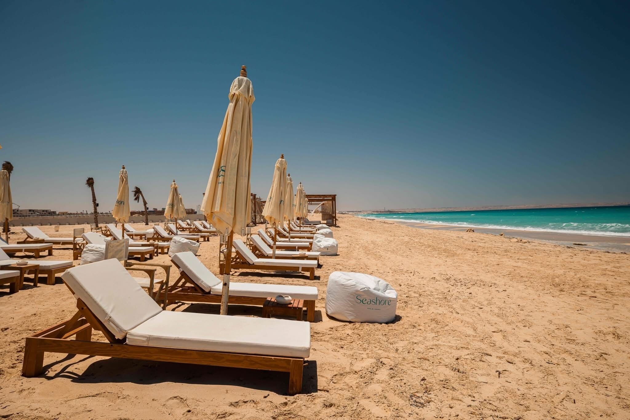 A beach with rows of sun loungers and umbrellas, a clear sky, and a calm sea.