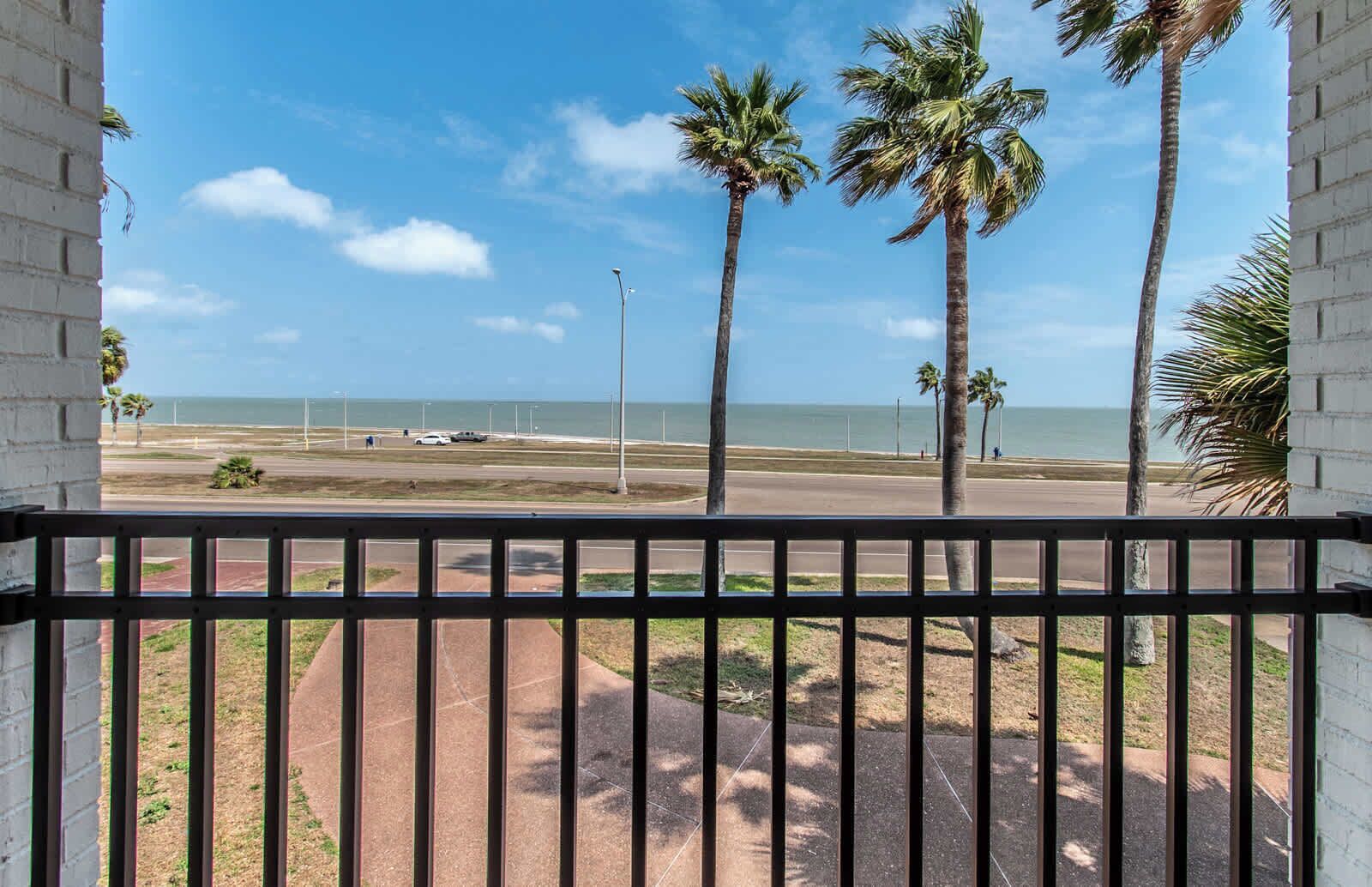 A balcony with a view of a beach, palm trees, and a clear sky.