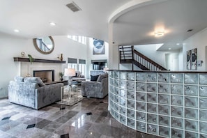 A spacious living room with a fireplace, a staircase, and a glass block wall. - Coastal Paradise Beachfront House - Sleeps 26 (Corpus Christi)