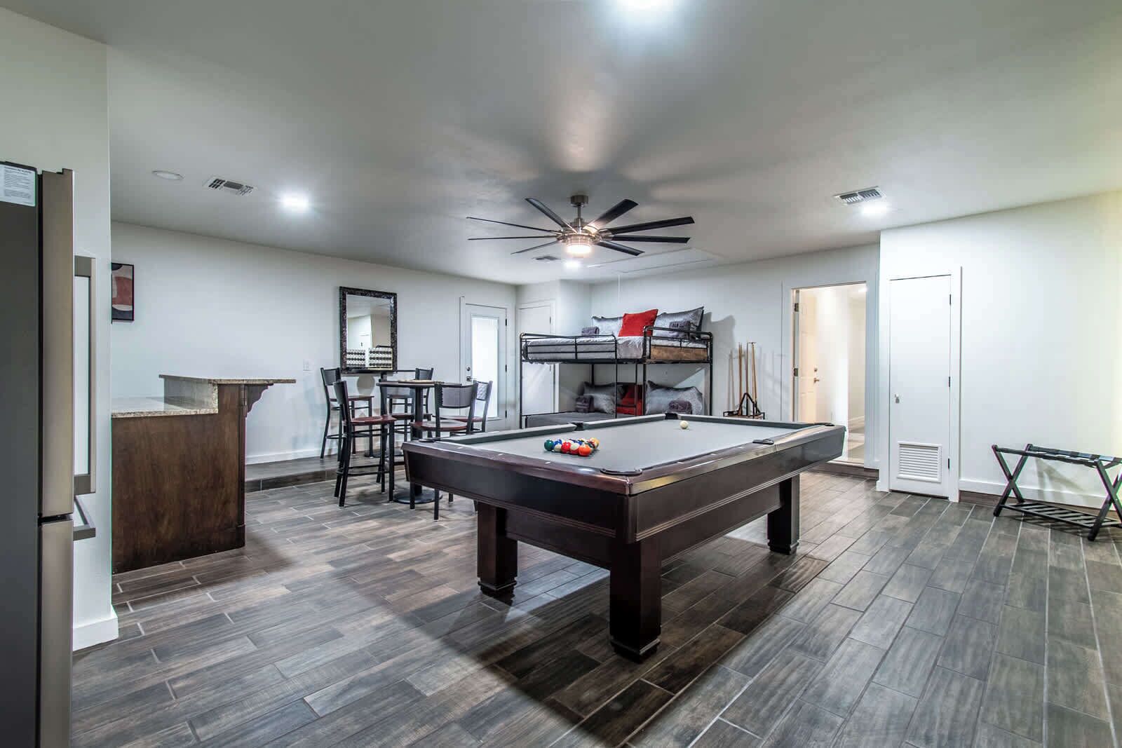 Une pièce équipée d’une table de billard, de lits superposés, d’un coin repas et d’un ventilateur de plafond.