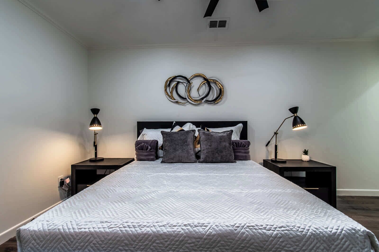 Un dormitorio con una cama grande, dos mesitas de noche, una lámpara de pared y un adorno en la pared.