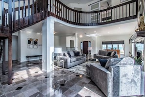 A spacious living area with a high ceiling, a staircase, and a view of the ocean. - Coastal Paradise Beachfront House - Sleeps 26 (Corpus Christi)