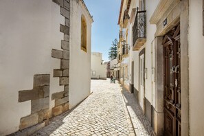 A narrow cobblestone street flanked by buildings with white walls and wooden doors.