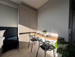 Habitació moderna amb llit, taula de dinar amb cadires, una planta petita i una finestra.