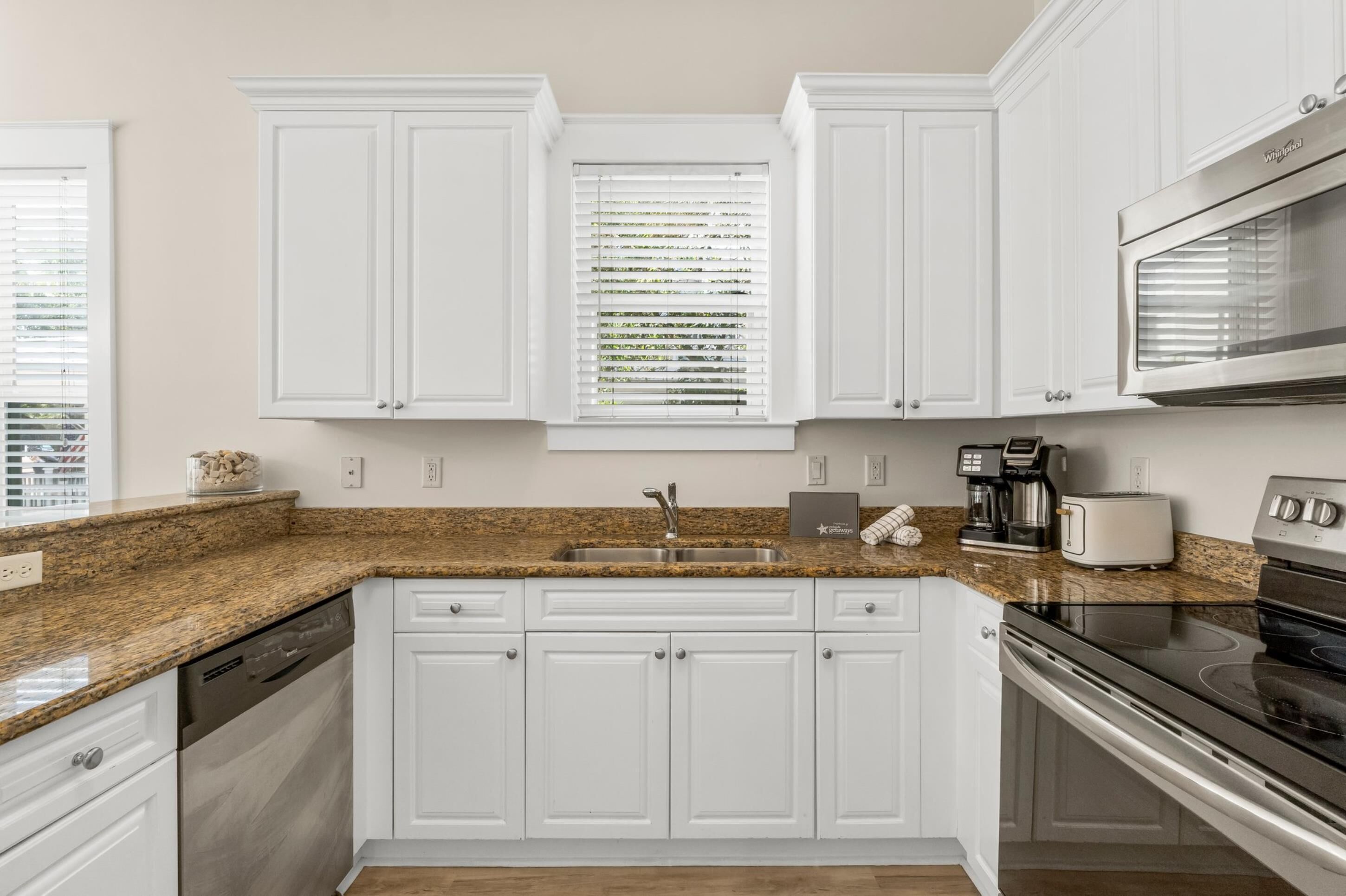 A kitchen with white cabinets, a granite countertop, a stainless steel sink, a toaster, a coffee maker, and a microwave.