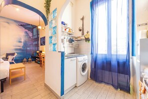 Ett kompakt bostadsutrymme med tvättmaskin, en matplats med bord och stolar samt en väggmålning.