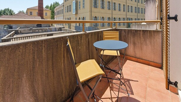 Uma varanda com mesa e cadeira, vista de um edifício com várias janelas e uma chaminé ao fundo.