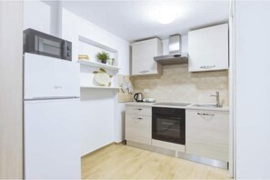 Een kleine keuken met witte kasten, een magnetron, een fornuis en een vaatwasser.