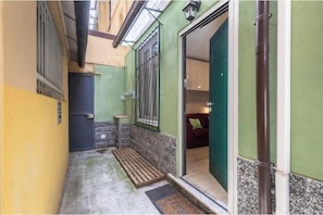 Un pasillo estrecho con una puerta que da a una habitación, una pequeña mesa y un banco.