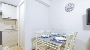 A compact kitchen with a dining table set for four, a clock on the wall, and a white cabinet. - Hostdomus - Lizzie's House (Alassio)
