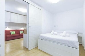 Een witte kamer met een bed, een rode bank en een garderobe.