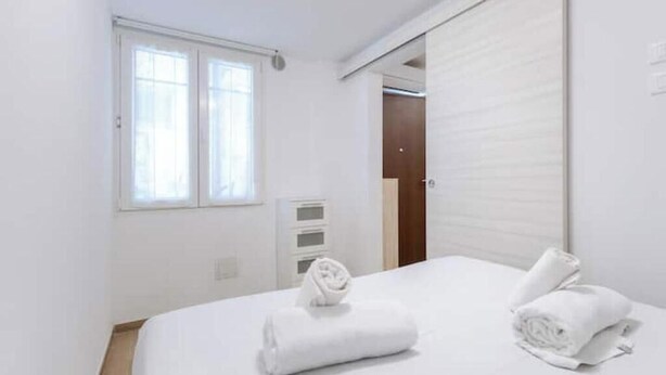 A hotel room with a bed, a window, a door, and a small cabinet. - Hostdomus - Lizzie's House (Alassio)