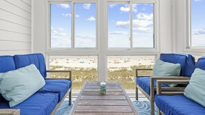 Habitación con vista a la playa, con un sofá azul, una mesa de madera y un ventanal con vistas a la playa.