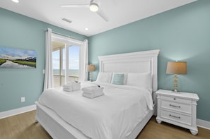 A bedroom with a large bed, white nightstands, and a view through an open door.
