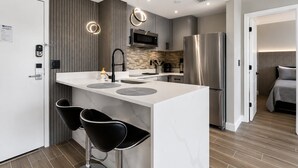 Une cuisine moderne dotée d’un îlot central, de deux tabourets de bar, d’un réfrigérateur en acier inoxydable et d’un four à micro-ondes.