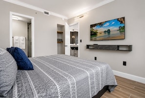 Ein Schlafzimmer mit Bett, einem Bild, einem Regal und einem durchgegangenen Tür sichtbar liegenden Badezimmer.