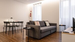 A modern living room with a grey sofa, a small round table, a desk with a computer, and a chair. - Cozy Figueira Apartment (Figueira da Foz)